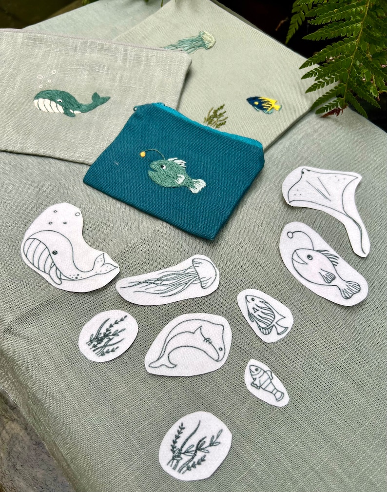 May include: A set of 10 iron-on patches featuring various sea creatures, including whales, fish, jellyfish, and seaweed. The patches are white with black embroidery and are perfect for adding a nautical touch to clothing, bags, or other fabric items.