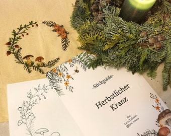 May include: A beige tote bag with an embroidered wreath design, a green wreath with a lit candle, and a guide titled "Herbstlicher Kranz". The guide features illustrations of plants and mushrooms.