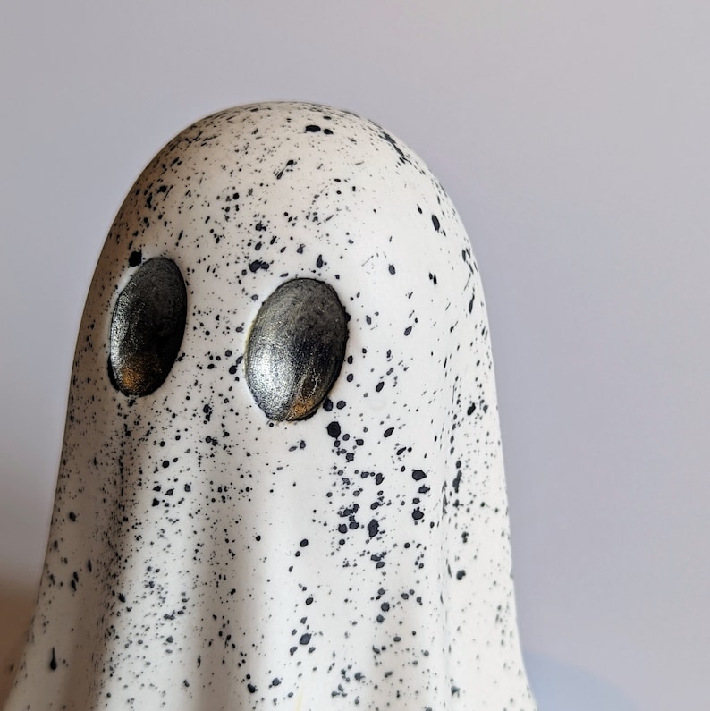 May include: White ceramic ghost figurine with black speckles and silver eyes.