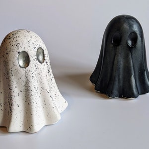 May include: Two ceramic ghost figurines, one white with black speckles and silver eyes, the other black with silver eyes.