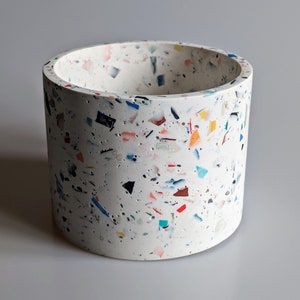 May include: White cylindrical planter with a speckled surface made from recycled materials. The planter is filled with colourful flecks of various sizes and shapes.