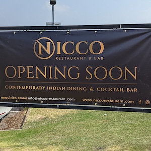 May include: A black sign with gold lettering announcing the opening of a restaurant called "Nicco" with the tagline "Contemporary Indian Dining & Cocktail Bar". The sign also includes the restaurant's website and email address.