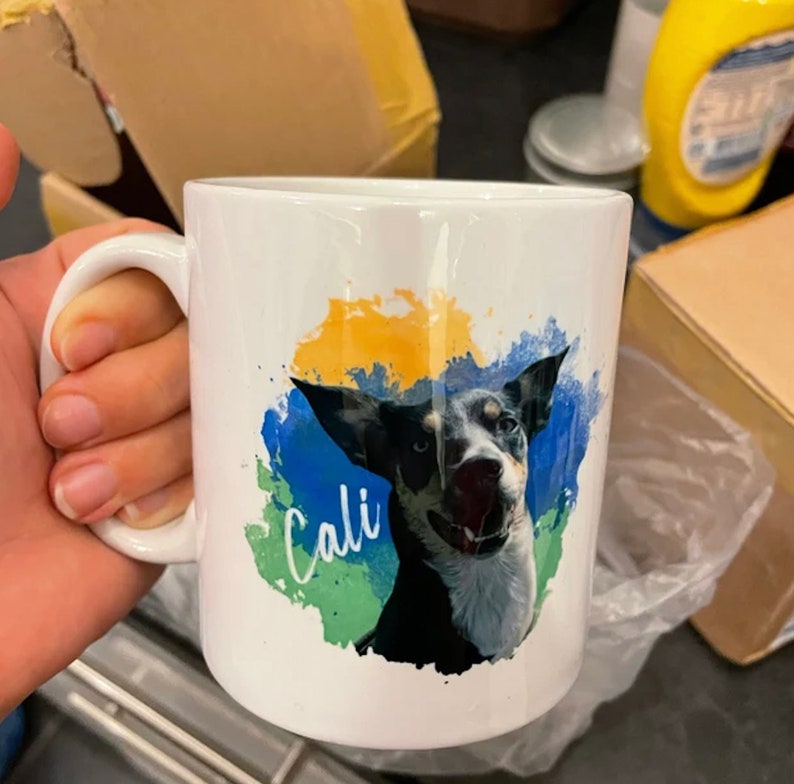 May include: White ceramic mug with a colourful watercolour design featuring a black and white dog with the name "Cali" written in cursive.