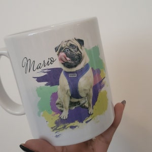 May include: White ceramic mug with a colourful abstract design featuring a pug dog wearing a purple harness. The dog's name, "Mario", is written in black cursive on the mug.