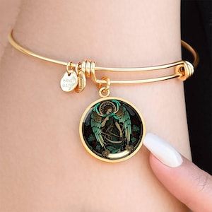 Peut inclure: Bracelet jonc doré avec un pendentif rond représentant un ange. Le pendentif a un fond noir avec des accents verts et sarcelle. Le bracelet a un charme qui dit "Hand Made".