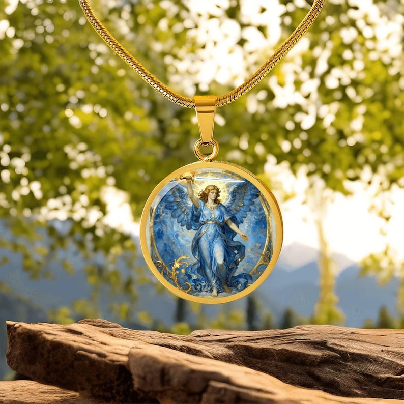K&ouml;nnte beinhalten: Vergoldete Halskette mit Anh&auml;nger, die einen runden Anh&auml;nger mit einer Illustration eines himmlischen Engels in Blau- und Goldt&ouml;nen zeigt. Der Engel ist mit Fl&uuml;geln und einem Schwert dargestellt. Die Halskette hat eine zarte Kette.