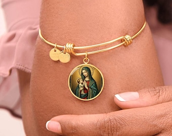 May include: Gold-tone bangle bracelet featuring a round pendant with a religious image of Mary and baby Jesus. The pendant is framed in gold and hangs from the bracelet. Two small, round charms are also attached to the bracelet.
