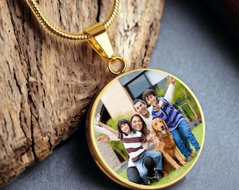 May include: A gold-colored pendant necklace with a round charm displaying a family portrait with a dog. The necklace is on a wooden surface. The pendant has a gold-colored chain.