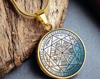 May include: A gold-toned circular pendant necklace featuring a complex geometric design with black text and symbols. The center displays a star pattern with planetary names and sigils, surrounded by the names Gabriel, Tzadkiel, Samael, Raphael, Haniel, and Michael.