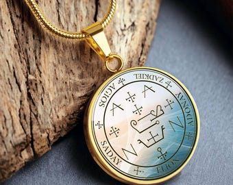 May include: Gold pendant necklace with a round, silver-colored charm featuring a complex geometric design and the words "SADAY", "ELION", "ZADKIEL", and "ADONAY".