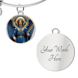 May include: Silver-toned charm bracelet with two round pendants. One pendant features an illustration of an angel in blue robes, holding a sword. The other pendant is blank with the words "Your Words Here" in cursive.