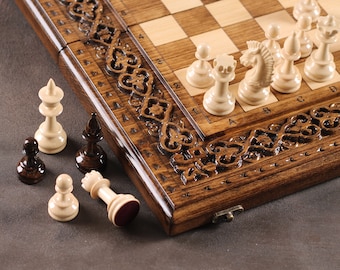 May include: A wooden chessboard with intricate carvings around the edge. The board is open and shows white chess pieces on the board and black and white chess pieces off the board.