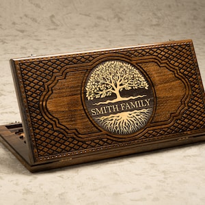 以下が含まれることがあります： 彫刻が施された木製のゲームボックス。生命の木の画像と「Smith Family」の文字が刻まれています。