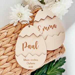 May include: Two wooden Easter egg ornaments with the names "Emma" and "Paul" engraved on them. The ornament with "Paul" also has the text "Mein erstes Ostern 2022" engraved on it.