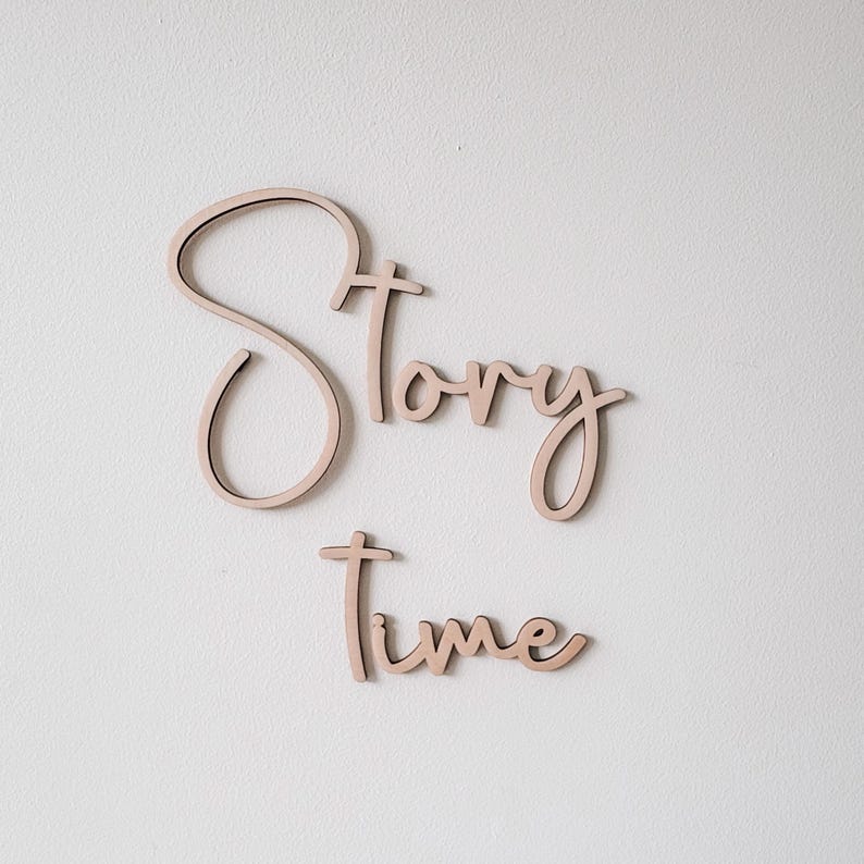 以下が含まれることがあります： 木製の壁飾りで、筆記体で「Story Time」と書かれています。文字は明るい自然な木の色で、言葉は装飾的に配置されています。子供部屋に最適です。