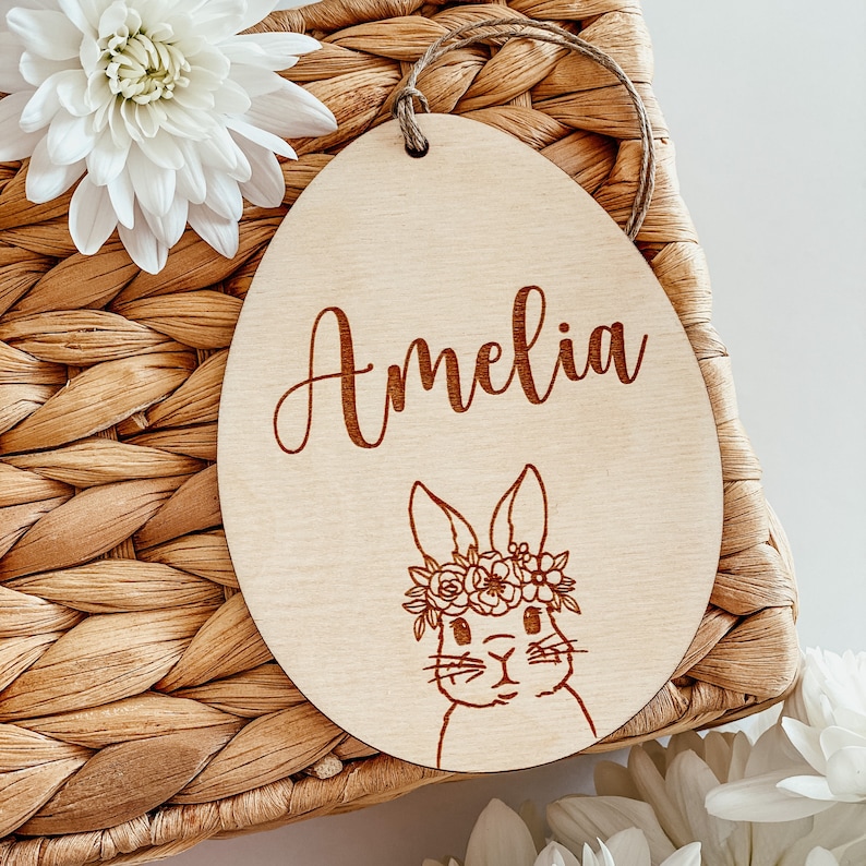 May include: A wooden Easter egg ornament with a bunny wearing a flower crown and the name Amelia engraved on it.