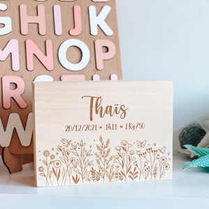 May include: A light-colored wooden box with the name "Tha&iuml;s" engraved on the top. Below the name are the date, time, and weight. The bottom of the box features an engraved floral design with flowers and butterflies.