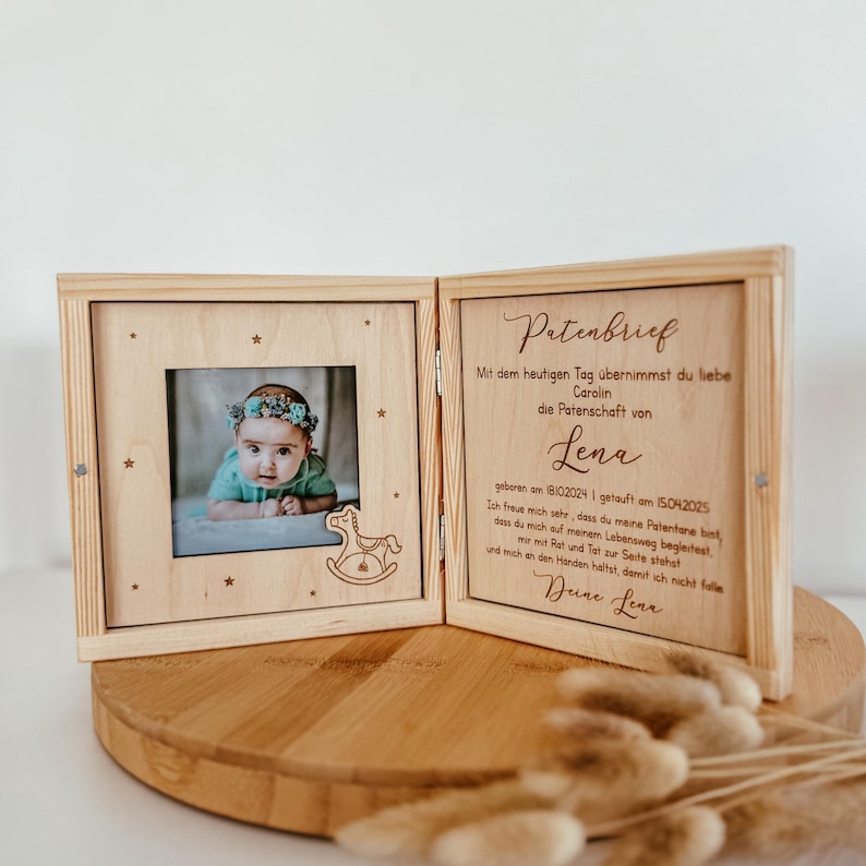 May include: A wooden box with a hinged lid, engraved with the text "Patenbrief". The box contains a photo of a baby girl and a rocking horse. The text reads: "Mit dem heutigen Tag &uuml;bernimmst du liebe Carolin die Patenschaft von Lena geboren am 18102024 1 getauft am 15042025 Ich freue mich sehr, dass du meine Patentane bist, dass du mich auf meinem Lebensweg begleitest, mir mit Rat und Tat zur Seite stehst und mich an den Handen h&auml;ltst, damit ich nicht falle Deine Lena"