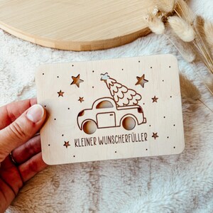 K&ouml;nnte beinhalten: Eine hellfarbene Weihnachtskarte aus Holz mit einem Ausschnitt-Design. Die Karte zeigt ein Auto, das einen Weihnachtsbaum, Sterne und den Text "KLEINER WUNSCHERF&Uuml;LLER" tr&auml;gt. Die Karte ist rechteckig mit abgerundeten Ecken.