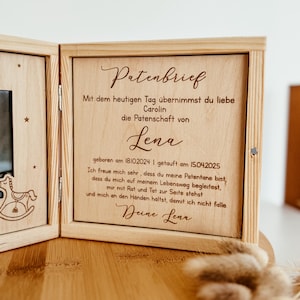May include: A wooden box with a photo frame and a message inside. The message reads "Patenbrief" and includes the text "Mit dem heutigen Tag &uuml;bernimmst du liebe Carolin die Patenschaft von Lena geboren am 18102024 | getauft am 15.04.2025 Ich freue mich sehr, dass du meine Patentane bist, dass du mich auf meinem Lebensweg begleitest, mir mit Rat und Tat zur Seite stehst und mich an den Handen haltst, damit ich nicht falle Deine Lena".