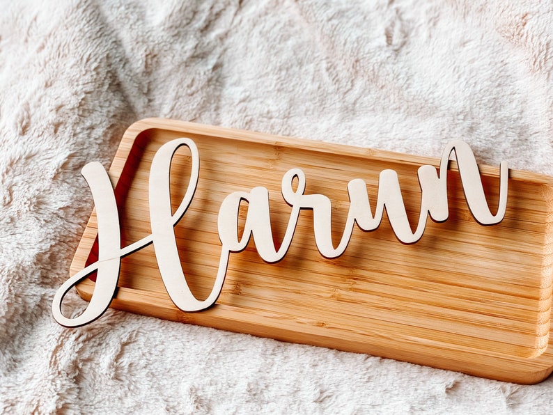 Puede incluir: Una bandeja de madera con el nombre "Harun" escrito en cursiva. La bandeja es de madera marr&oacute;n claro y tiene un acabado natural.