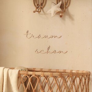 K&ouml;nnte beinhalten: Ein Weidenkorb-Babybett mit einer wei&szlig;en Decke und einer Holzpuppe darin. An der Wand hinter dem Babybett h&auml;ngt ein Holzschild mit der Aufschrift "traum sch&ouml;n".