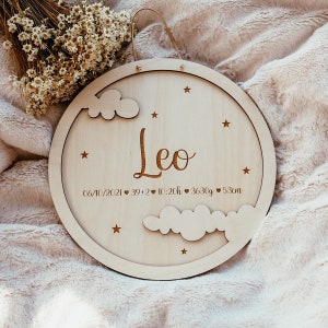 May include: A round wooden plaque with a cutout of clouds and stars. The plaque is engraved with the name "Leo", the date "06/10/2021", and the birth stats "39+2, 10:20h, 3630g, 53cm".