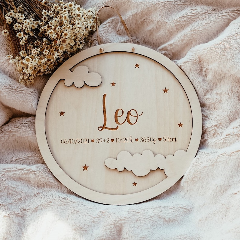 May include: A round wooden plaque with a cutout of clouds and stars. The plaque is engraved with the name "Leo", the date "06/10/2021", and the birth stats "39+2, 10:20h, 3630g, 53cm".