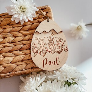 May include: A wooden Easter egg ornament with a floral design and the name "Paul" engraved on it. The ornament is light brown and has a white background.