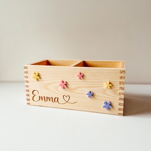 May include: A wooden box with two compartments, personalized with the name "Emma" and a heart. The box is decorated with colorful flowers.