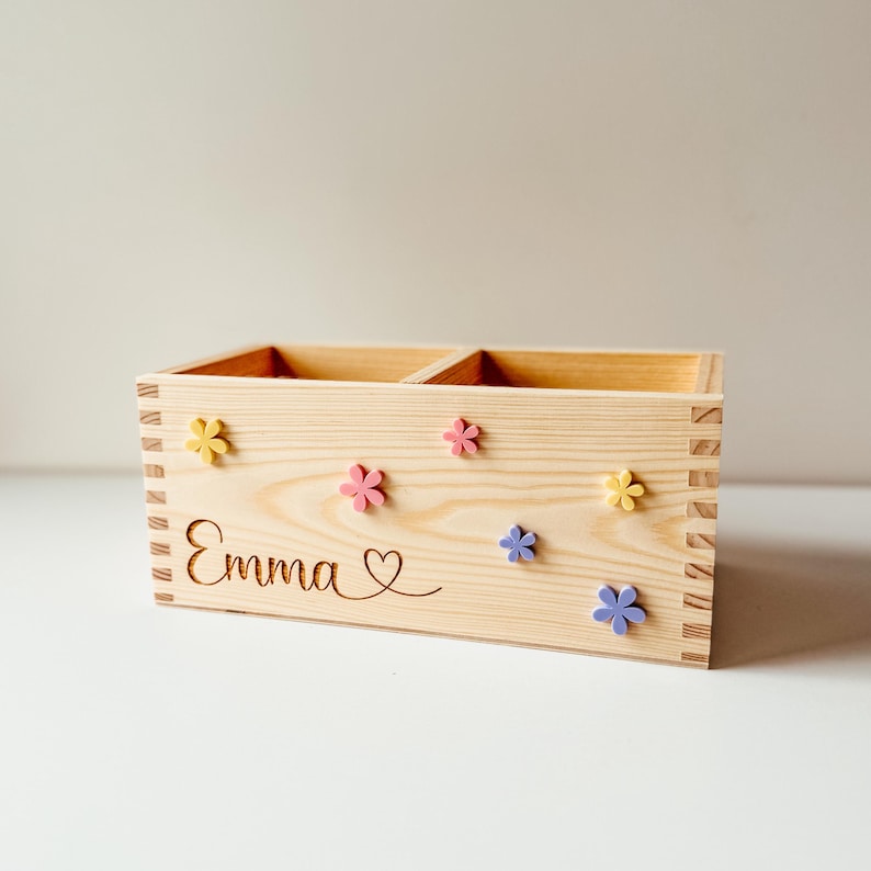 May include: A wooden box with two compartments, personalized with the name "Emma" and a heart. The box is decorated with colorful flowers.