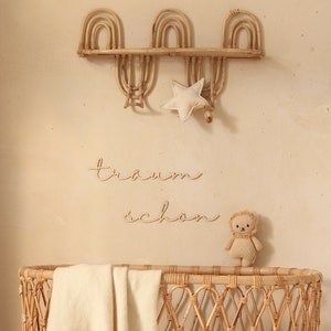 K&ouml;nnte beinhalten: Ein Weidenkorb-Babybett mit einer wei&szlig;en Decke und einem Stofftier-L&ouml;wen. Das Bett ist mit einem Holzschild verziert, auf dem "tr&auml;um sch&ouml;n" steht, und einem sternf&ouml;rmigen Kissen.