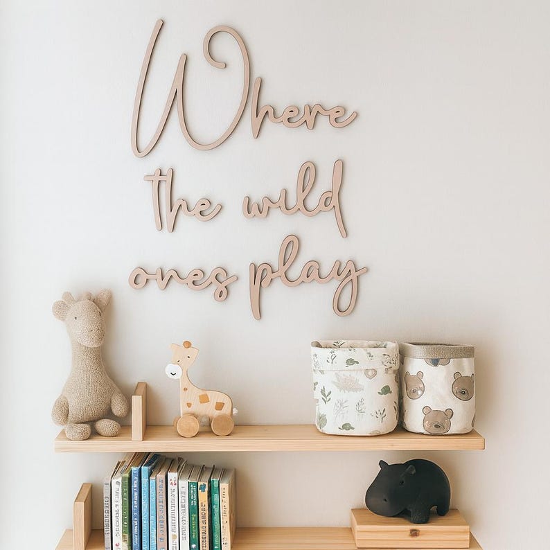May include: A nursery scene with wooden shelves displaying a stuffed giraffe, a wooden giraffe toy, two fabric storage bins, and a black hippo figurine. The wall features wooden script reading "Where the wild ones play."
