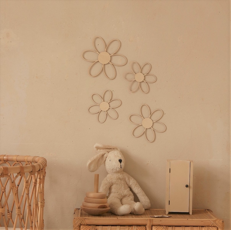 May include: A beige wall with four wooden daisy-shaped wall decor pieces. A stuffed bunny rabbit sits on a wooden table with a wooden stacking toy. A wicker basket and a small wooden cabinet are also on the table.