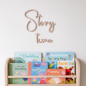Può includere: Una libreria in legno piena di libri per bambini, tra cui "The Duckling" e "Peppos Luntho." Sopra lo scaffale, le parole "Story Time" sono visualizzate in legno scritto.