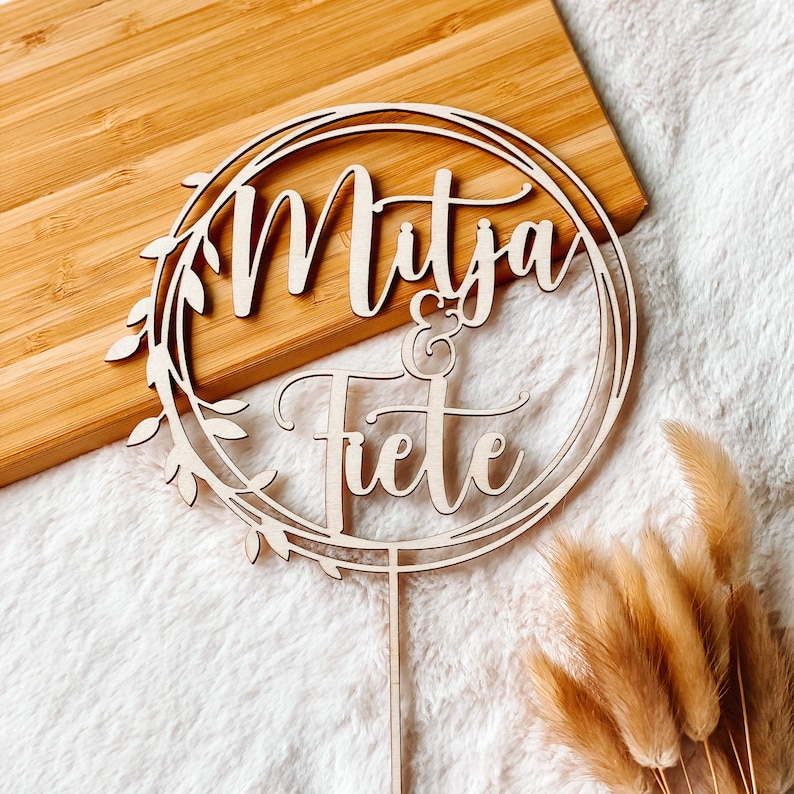 May include: Wooden cake topper with a circle design and the words "Mitja & Fiete" in cursive script.