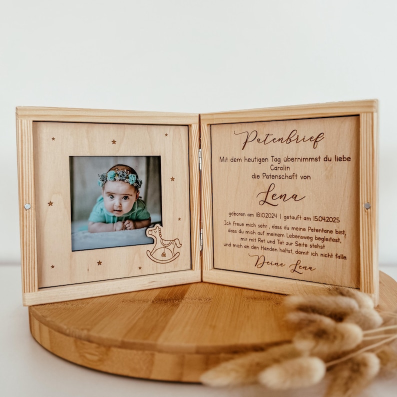 May include: A wooden box with a hinged lid, containing a photo of a baby and a handwritten letter. The letter is addressed to "Carolin" and states that she is taking on the role of godparent for "Lena", who was born on 18/10/2024 and baptized on 15/04/2025. The letter is signed "Deine Lena".