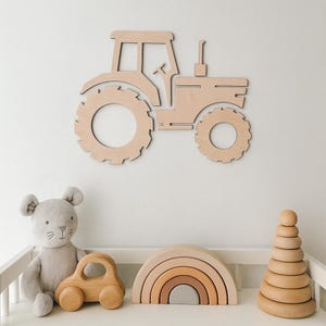 May include: A wooden tractor wall decor in a light brown color. The tractor has large wheels, a cab, and a smokestack. The image also shows a gray stuffed animal, a wooden car, a wooden rainbow, and a wooden stacking toy.