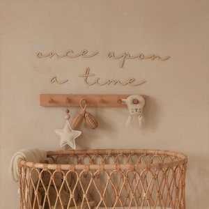 May include: A wooden sign with the words "once upon a time" in cursive script hangs on a wall above a wicker bassinet. The sign is decorated with a wooden rabbit toy and a star-shaped rattle.