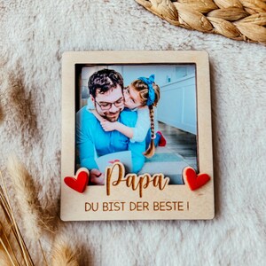 May include: A wooden photo frame with a picture of a father and daughter. The frame has two red hearts on the side and the text "Papa Du Bist Der Beste!" at the bottom.