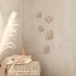 May include: A set of five wooden bee cutouts in various sizes, arranged on a light beige wall. The bees are all facing the same direction and have a simple, minimalist design.