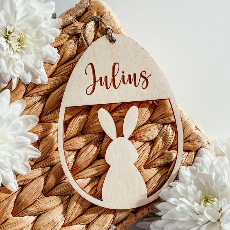 Op de afbeelding: Een houten paasei-versiering met de naam "Julius" erop gegraveerd. Het ei is versierd met een uitgesneden konijn.