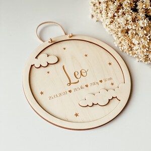 May include: A round wooden plaque with a cutout of clouds and stars. The plaque is engraved with the name "Leo", the date "25.01.2022", the time "21:54h", the weight "2810g", and the length "50cm".