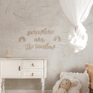 K&ouml;nnte beinhalten: Wanddekoration aus Holz mit dem Spruch "somewhere over the rainbow" und zwei Regenbogen-Ausschnitten. Die Dekoration ist an einer hellgrauen Wand in einem Kinderzimmer angebracht.