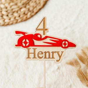May include: Red and white wooden race car cake topper with the number 4 and the name Henry.