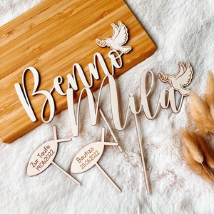 May include: Wooden cake toppers with the names "Benno" and "Mila" in cursive script. Two additional toppers feature doves with olive branches and the text "Zur Taufe 19.06.2022" and "Bautizo 25.06.2022".