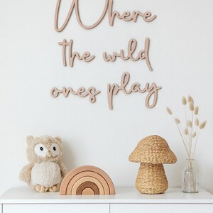 May include: A white chest of drawers with a wooden sign saying "Where the wild ones play." It's decorated with a stuffed owl, a wooden rainbow, a woven mushroom lamp, and a vase with dried flowers.