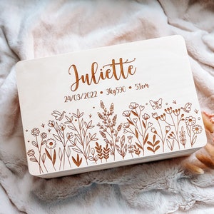 May include: A light-colored wooden box with the name "Juliette" engraved on the top. The box features an engraved floral design along the bottom edge and the date 03/24/2022, weight 3kg590, and height 51cm.