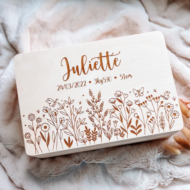 May include: A light-colored wooden box with the name "Juliette" engraved on the top. The box features an engraved floral design along the bottom edge and the date 03/24/2022, weight 3kg590, and height 51cm.