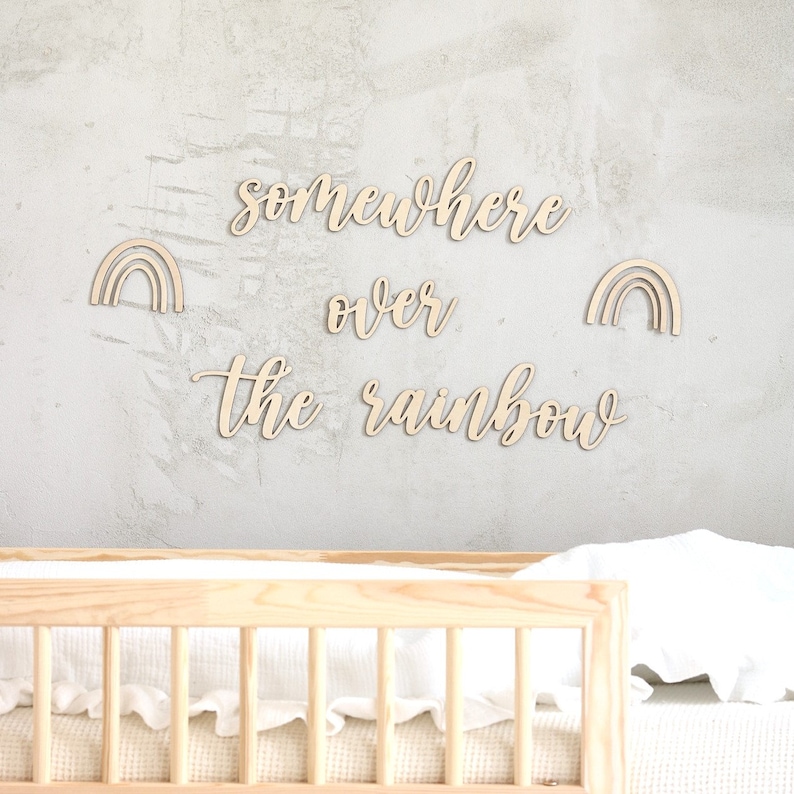 K&ouml;nnte beinhalten: Wanddekoration aus Holz mit dem Spruch "Somewhere over the rainbow" in Kursivschrift. Zwei ausgeschnittene Regenb&ouml;gen aus Holz sind ebenfalls enthalten.